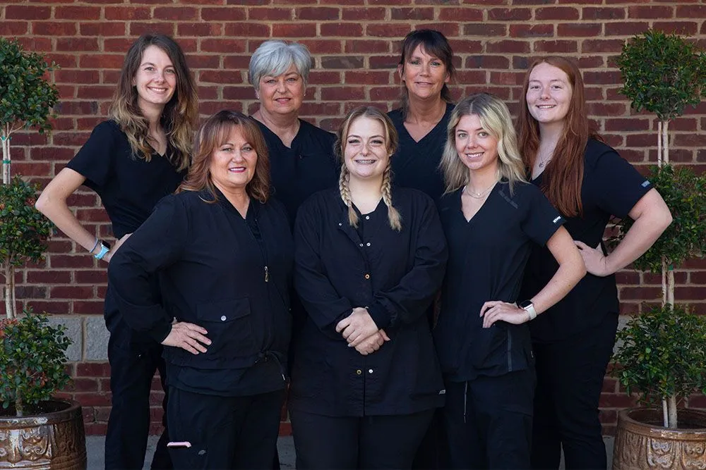 A group of the Independence Family Dentistry clinical team in black scrubs standing against the office's red-brick exterior.