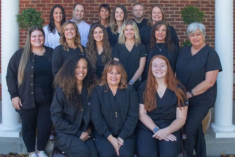The full Independence Family Dentistry team in black scrubs on the brick steps and white columns of the office